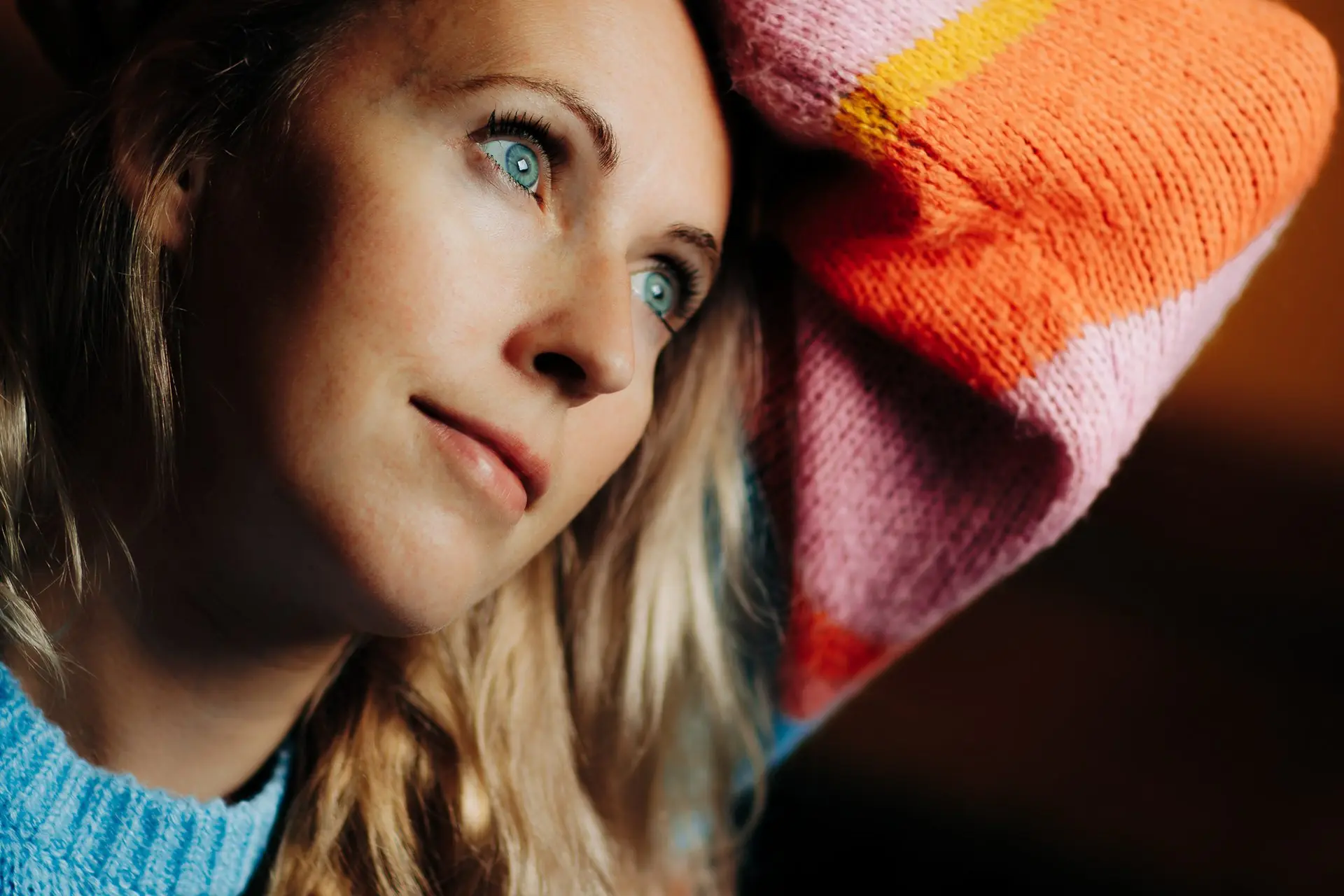 A woman with blue eyes looks up and away, a pink knitted blanket at her shoulder.