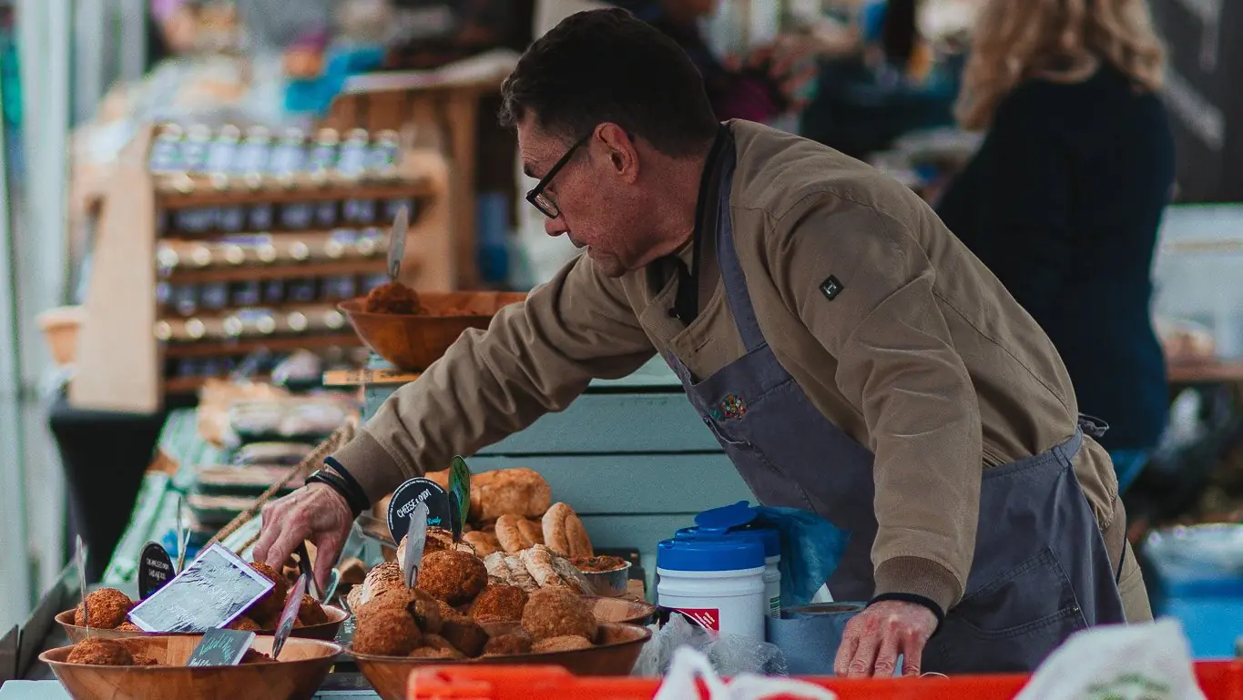 A baker arranges bread on a busy farmers' market stall.