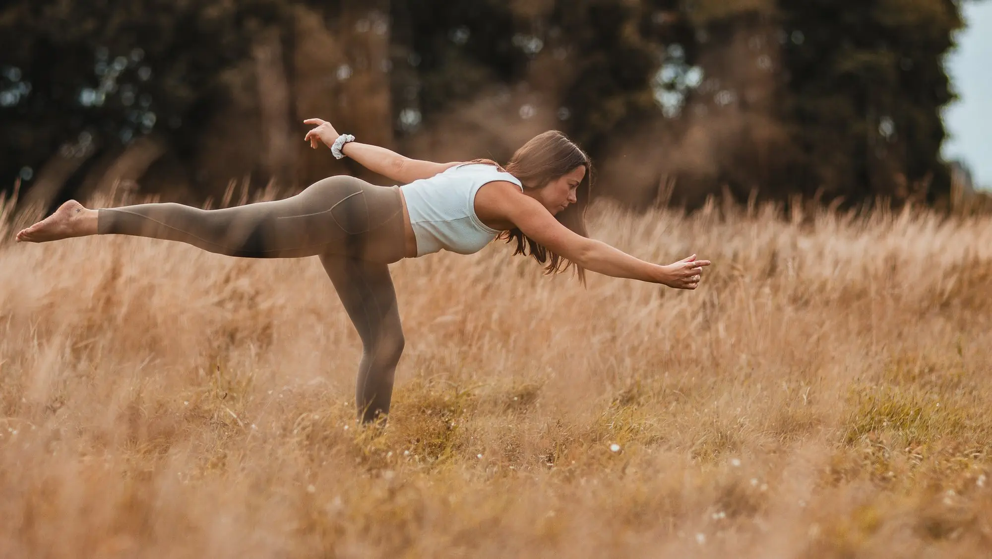 A woman balances in a yoga pose in a golden field of long grass.