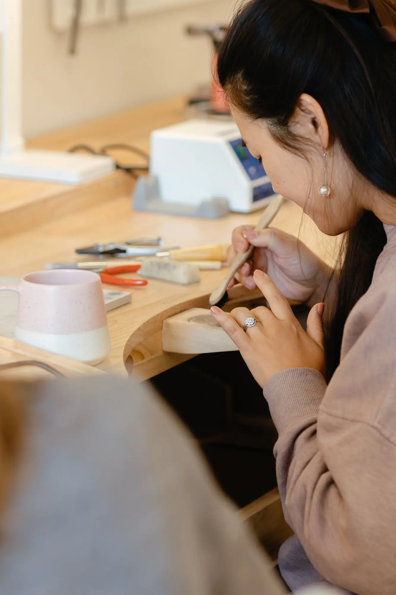 Woman works at a bench using jewellery-making tools.