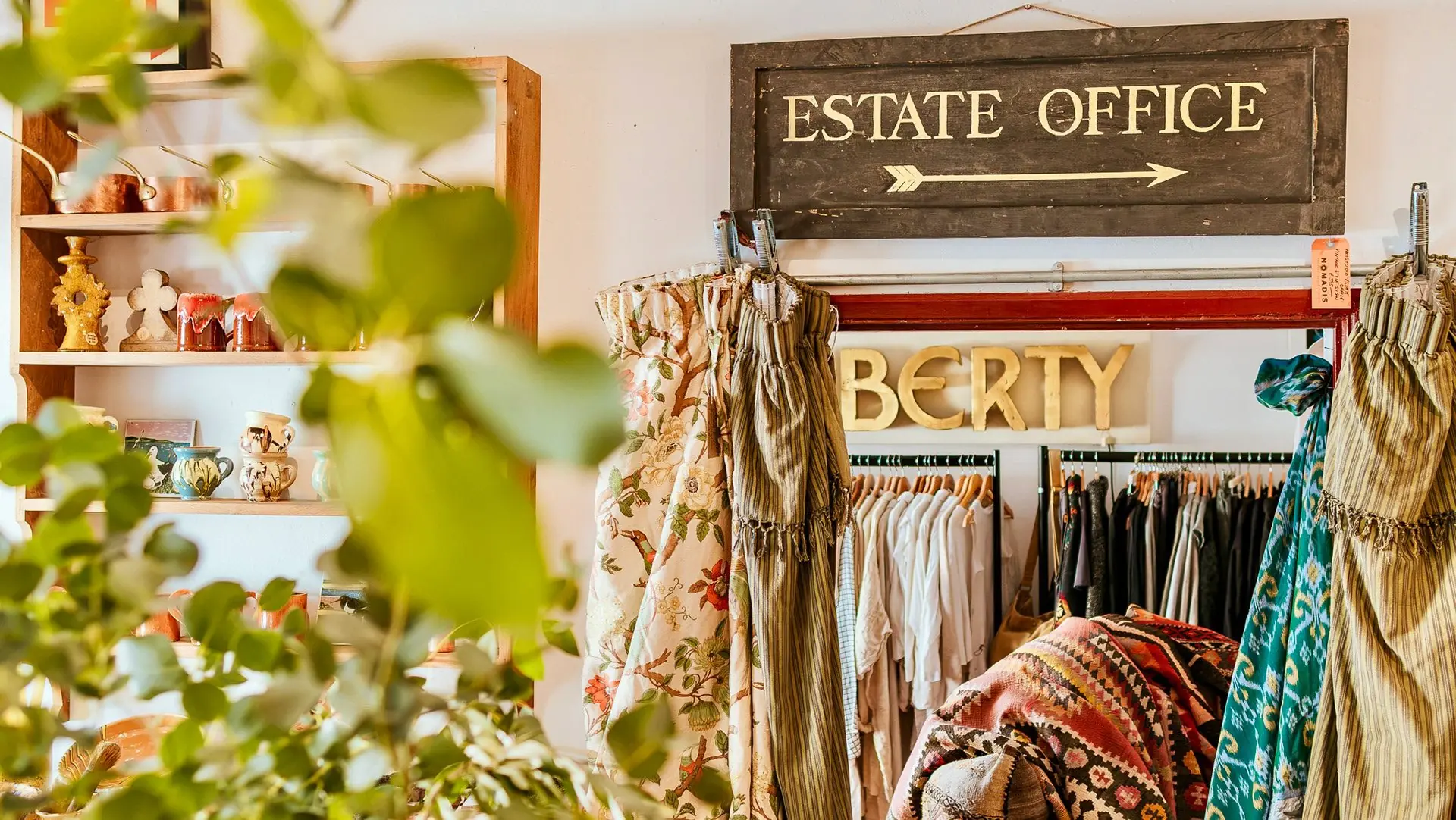 Vintage clothes, plants and an Estate Office sign inside a colourful shop.