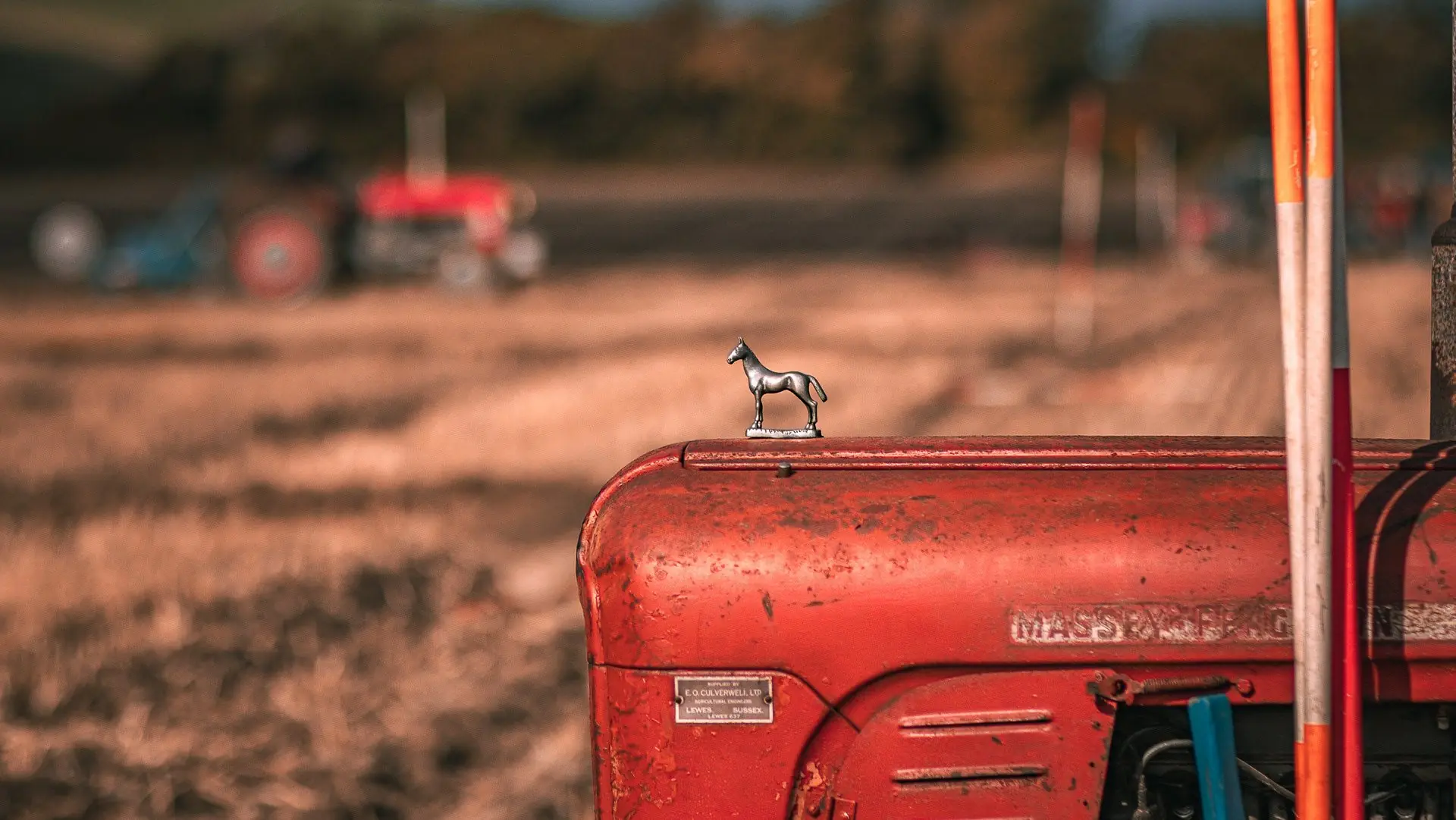 A small horse mascot on the bonnet of a red vintage tractor in a ploughed field.