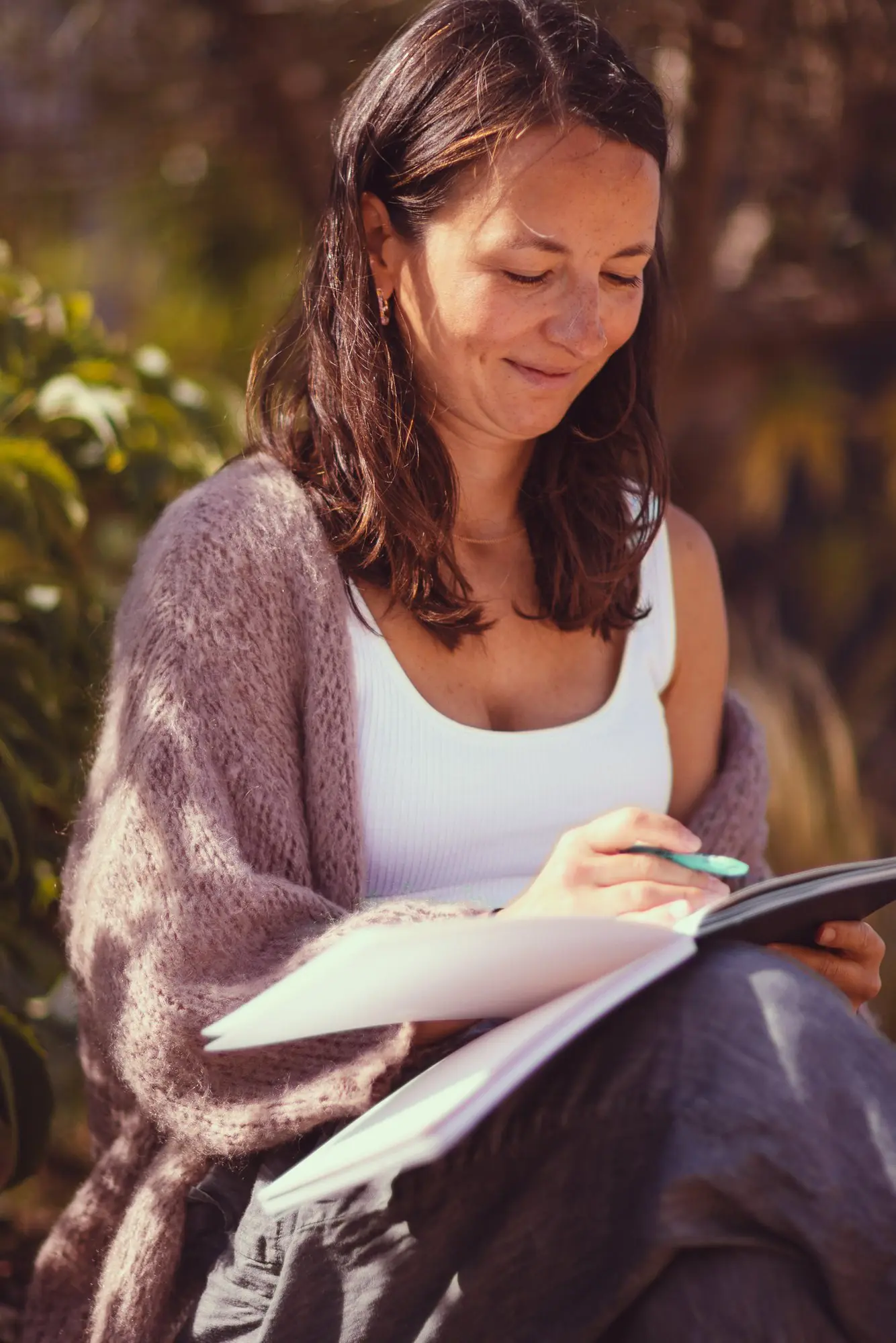 Woman writing in a notebook outdoors, dappled autumn light around her.