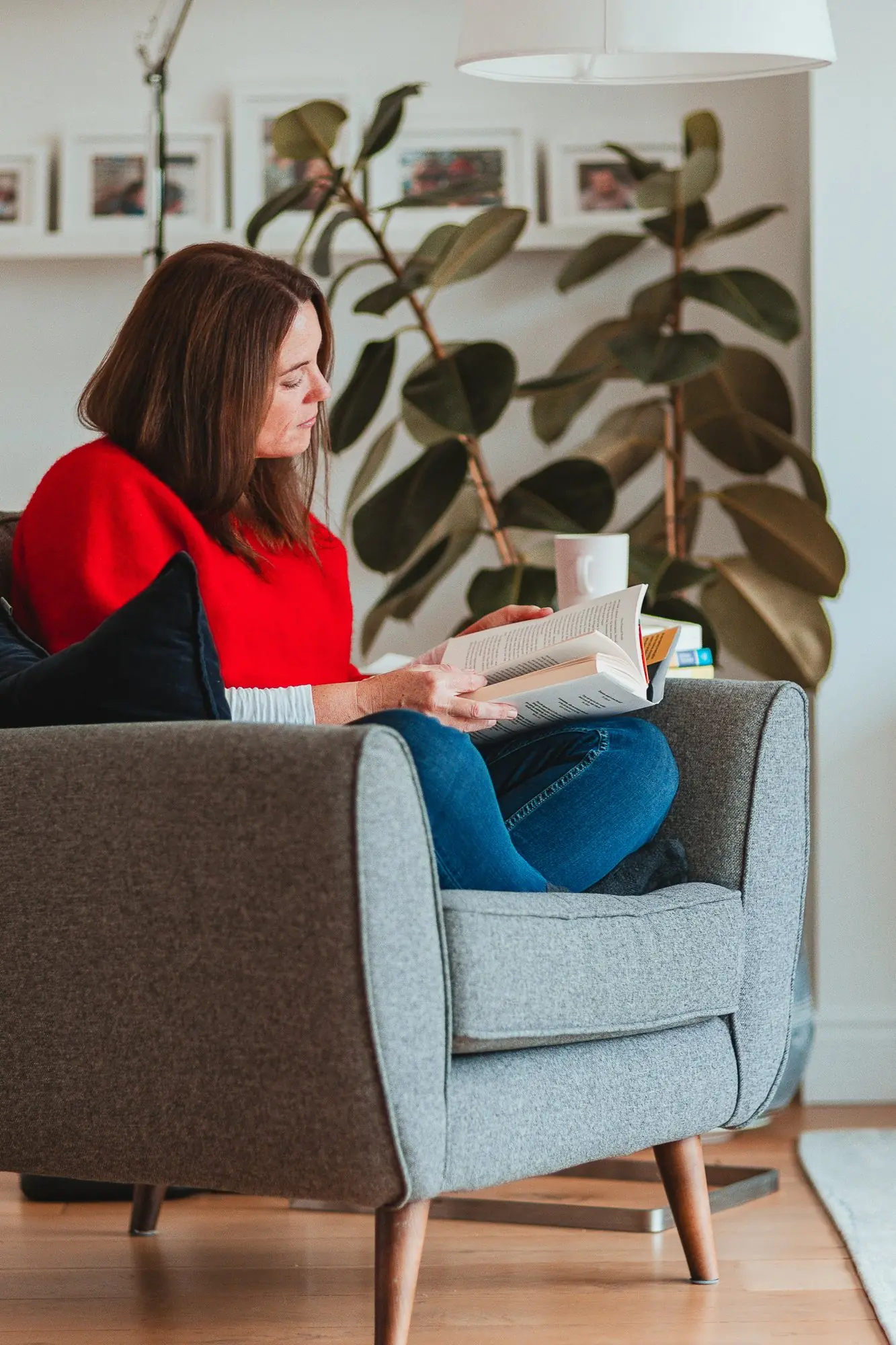 Woman curled up reading in an armchair beside a large houseplant.