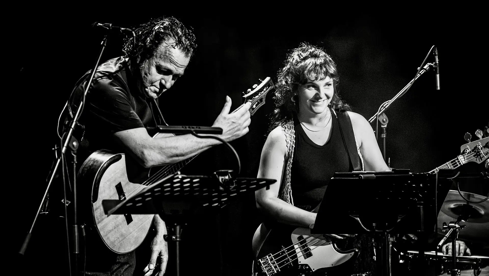 Black and white shot of two musicians smiling on stage with guitar and bass.